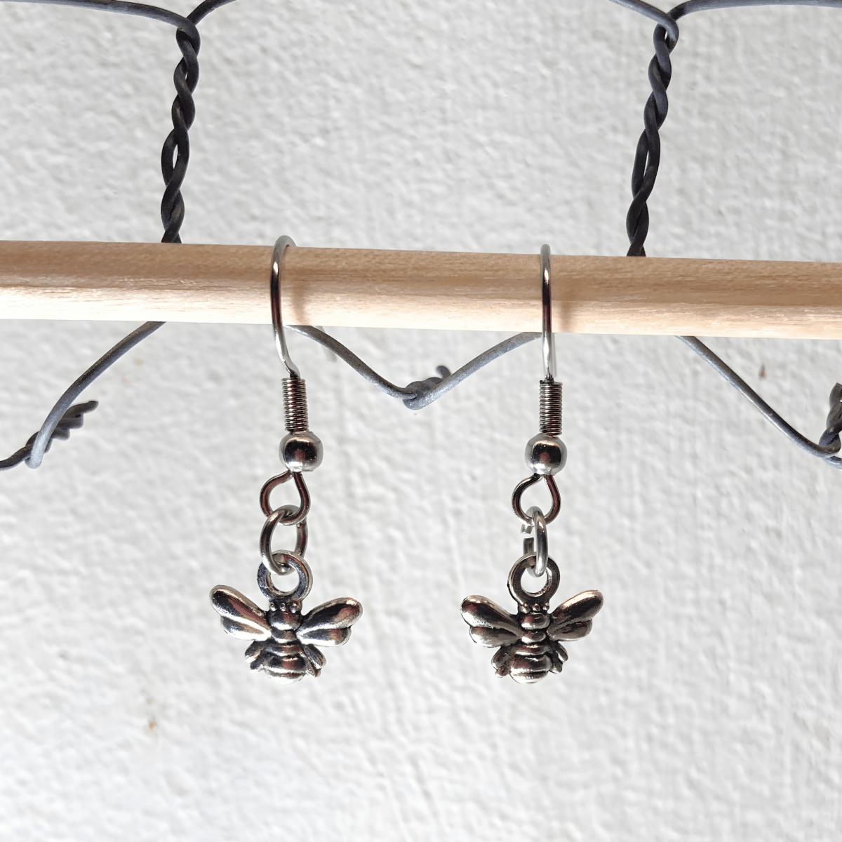 Silver bee-shaped earrings hanging from a wooden rod against a white background