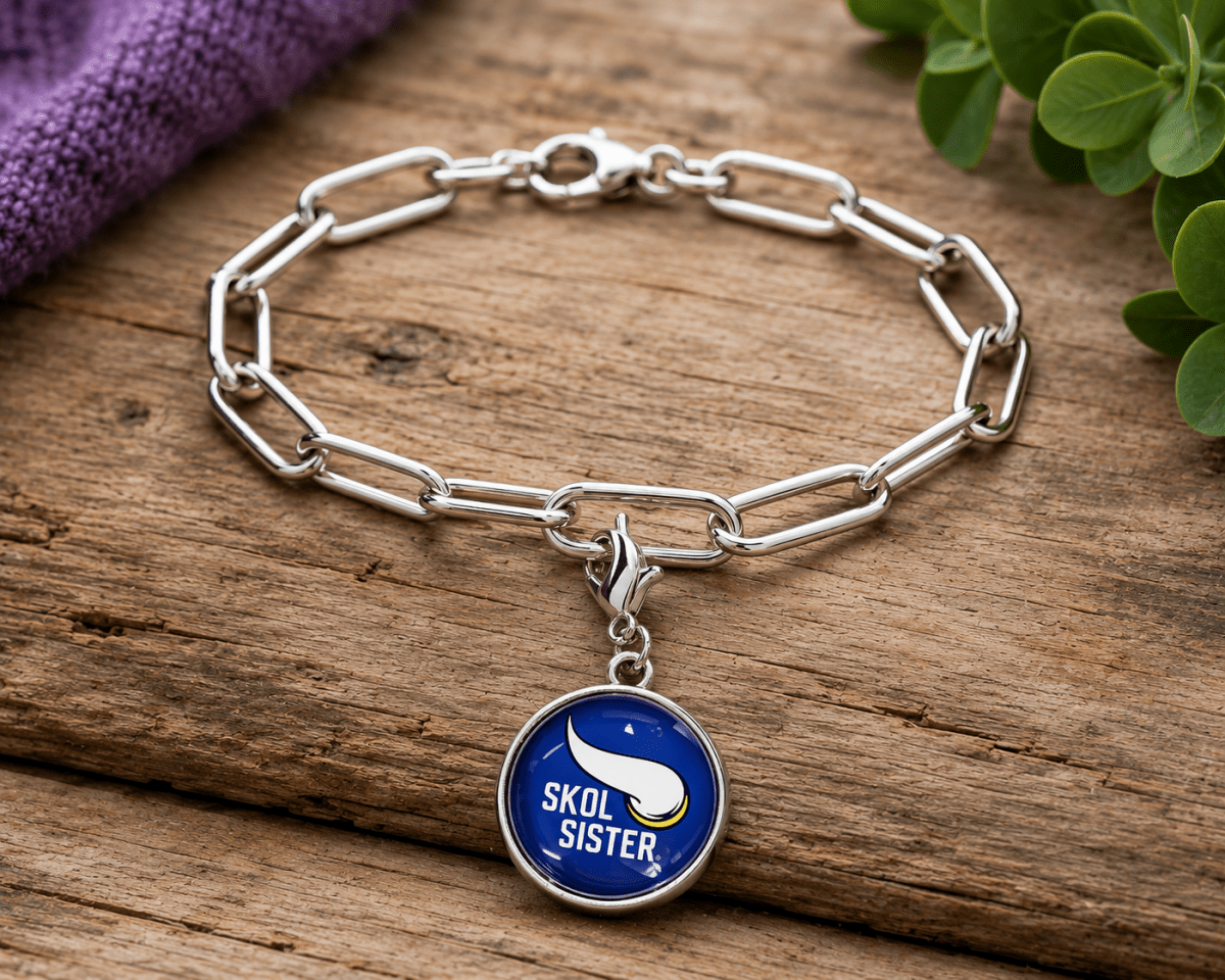 Silver chain bracelet with a blue 'SKOL SISTER' charm on a wooden surface.