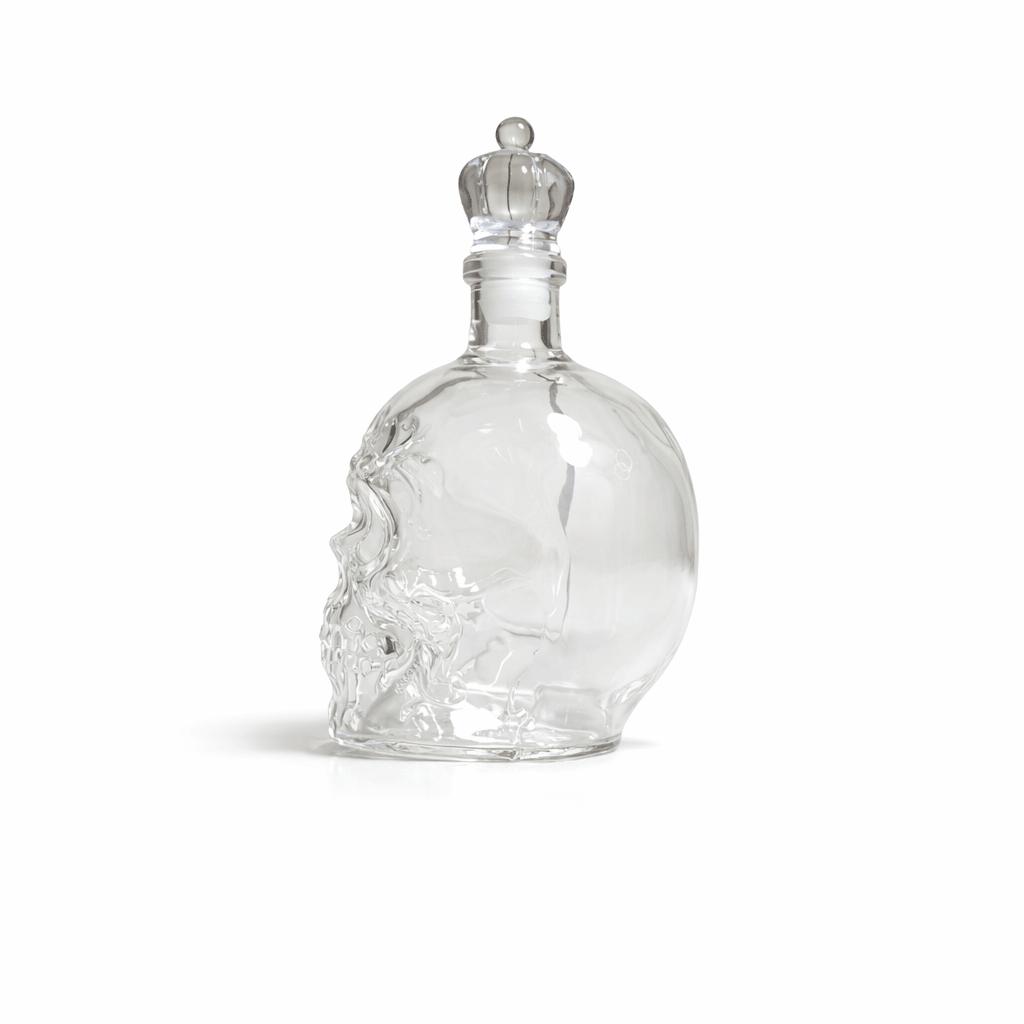 Clear glass skull-shaped bottle with a silver cap on a white background