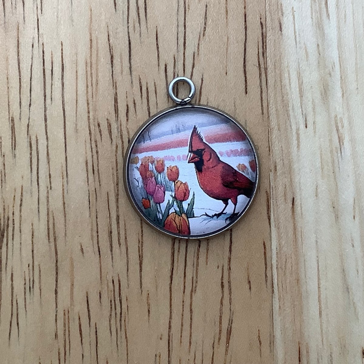 a charm of a cardinal standing in a snowy field of tulips emerging from the snow.