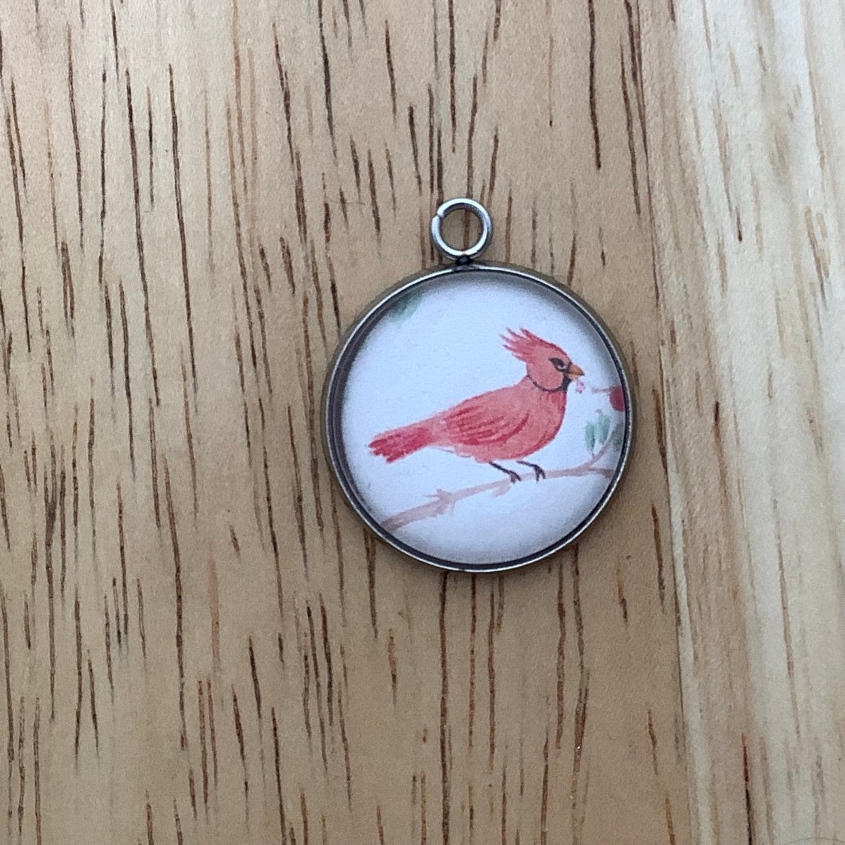 a charm of a color pencil drawing of a cardinal on a branch