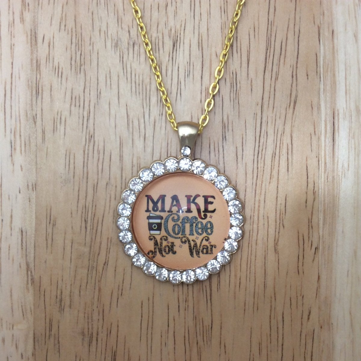 gold necklace with a gold jeweled glass cabochon pendant that says Make Coffee not war.