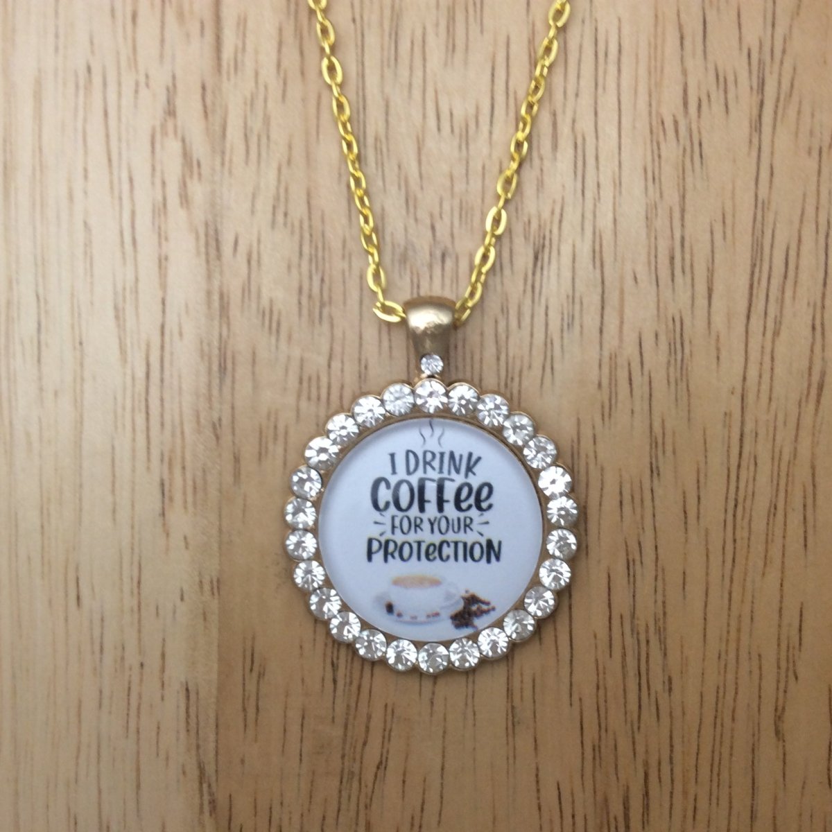 gold necklace with a gold jeweled glass cabochon pendant that says I drink coffee for your protection