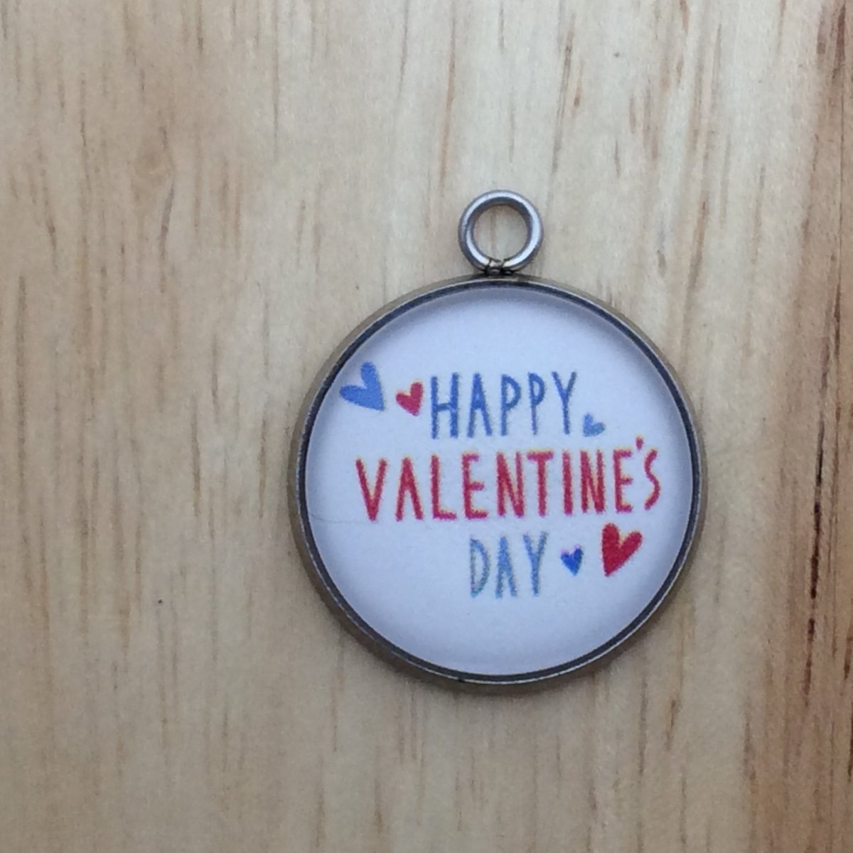 one glass cabochon charm with white background that has hearts and says happy valentines day in blue and red