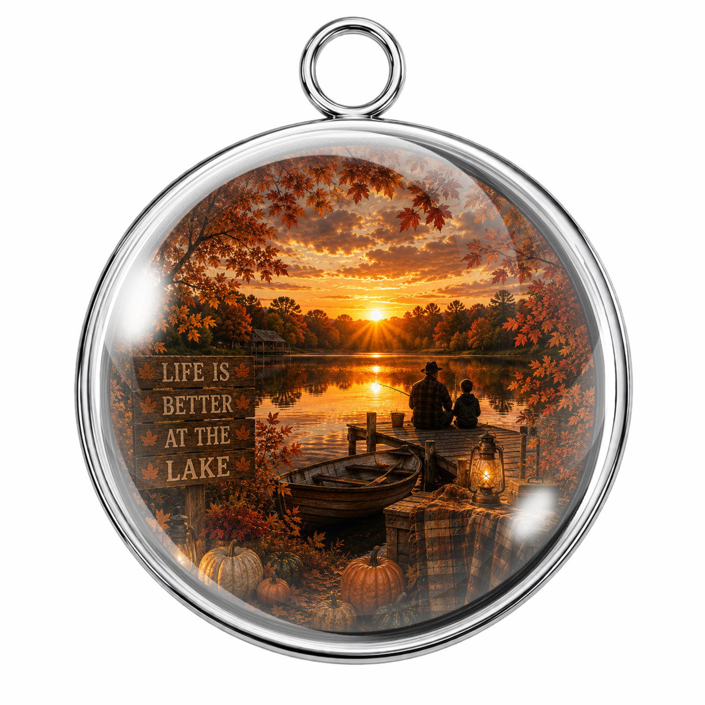 Round silver-toned pendant with a clear glass dome and a printed autumn lakeside sunset scene inside, featuring a dock, silhouetted figures, pumpkins, and a sign reading 'LIFE IS BETTER AT THE LAKE.'.