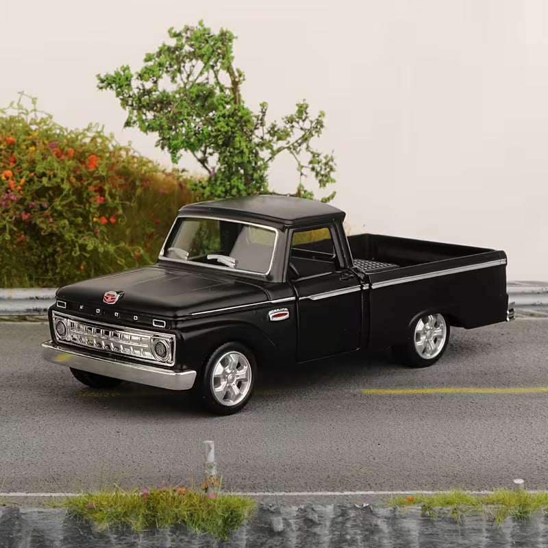 A black vintage pickup truck model with chrome details, displayed on a miniature gray road with a small tree and bushes in the background.