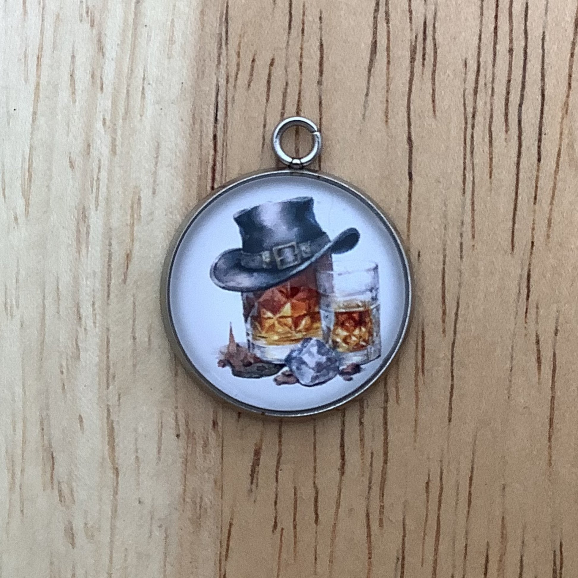 Charm depicting a bottle and a glass of brown liquor, the bottle has a cowboy hat covering the top.