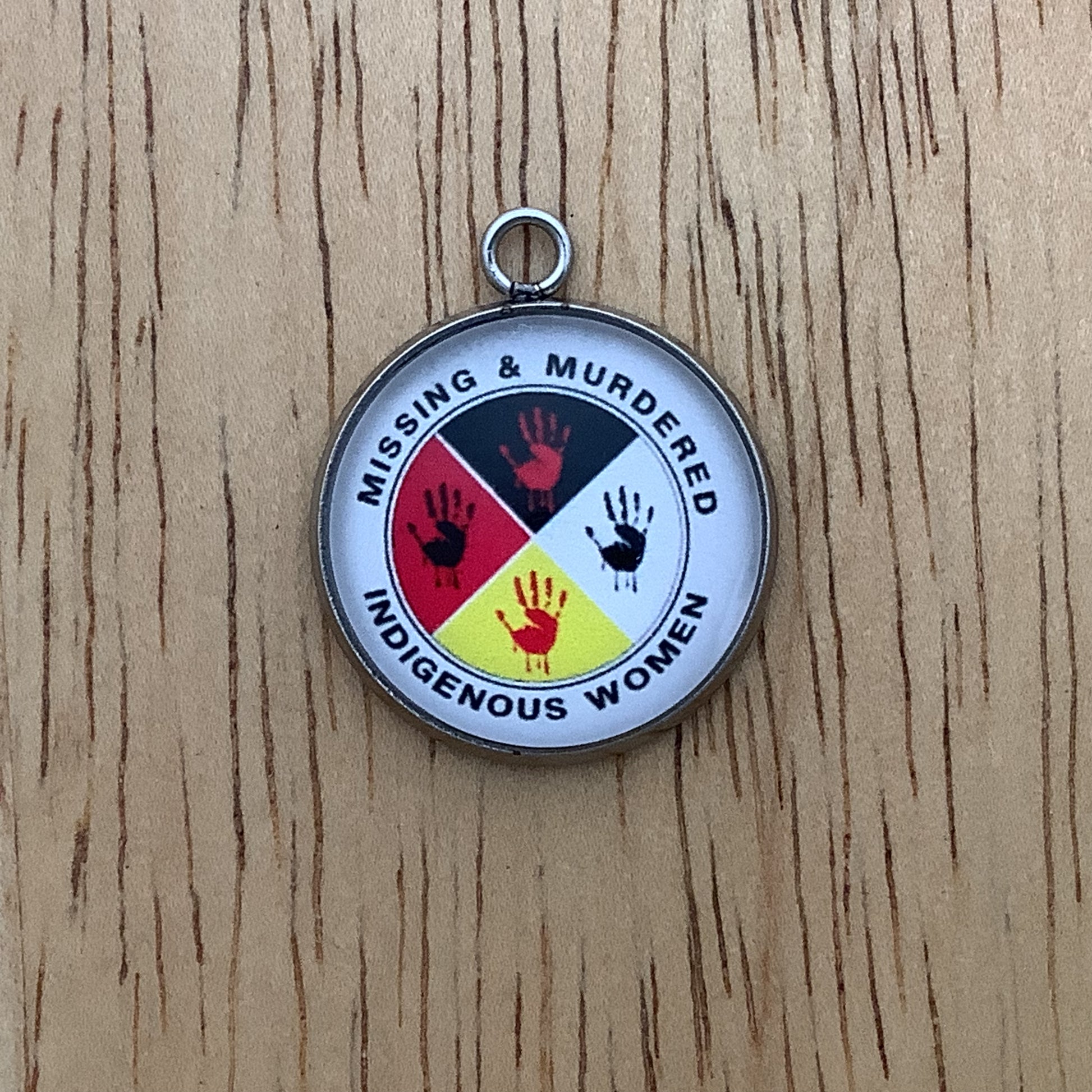 Missing & Murdered Indigenous Women written around a graphic of handprints in red and black inside a circle with colors of red, black white and yellow quarters.