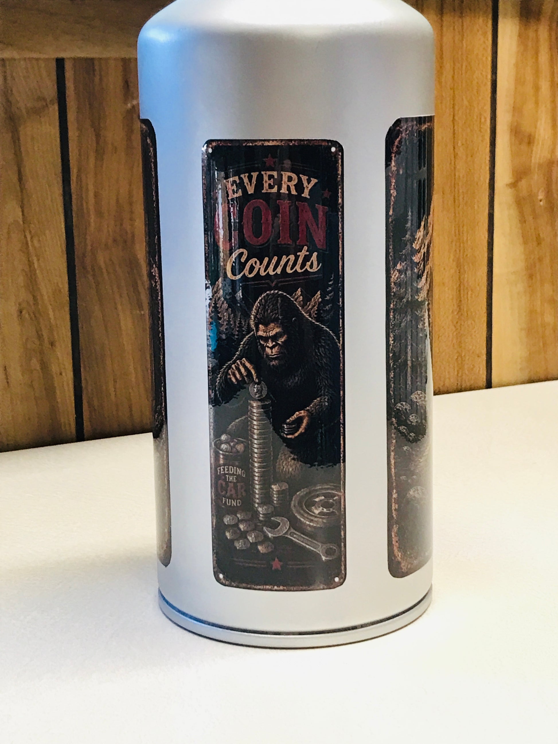 A white cylindrical coin jar with three vertical panels, featuring a central dark panel with an illustration of a giant ape and the text 'EVERY COIN Counts'.