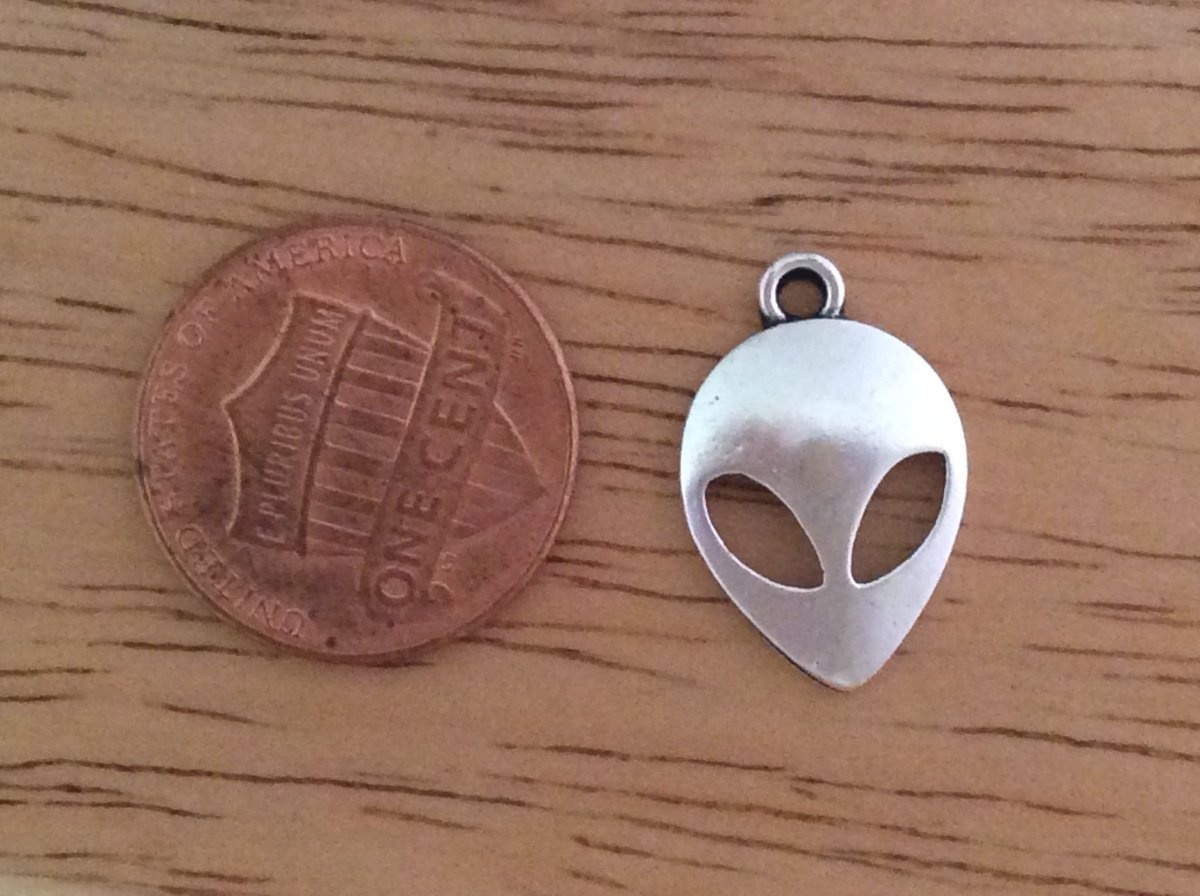 tibetan silver alien charm next to a Penney for size