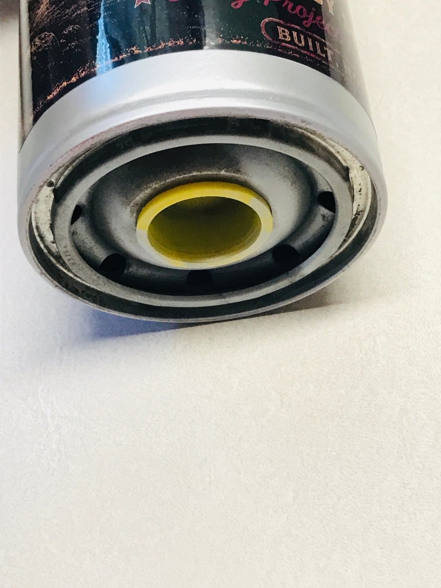 Close-up of the bottom end of a cylindrical metal canister, showing a silver rim, dark printed label, and a yellow circular insert on a white surface.