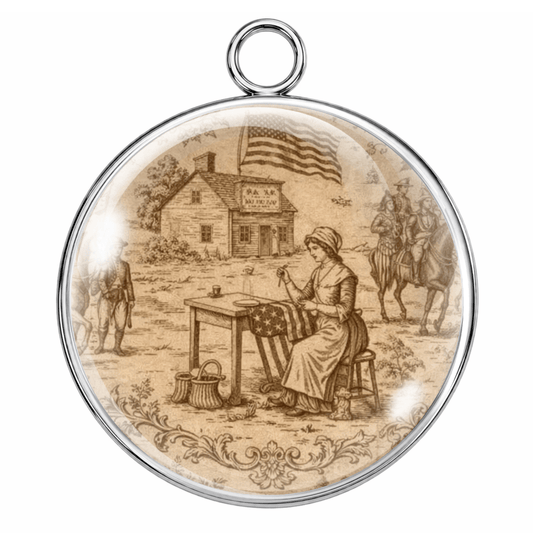 Round pendant with a vintage-style illustration of a woman sewing an American flag, with a house and people in the background.