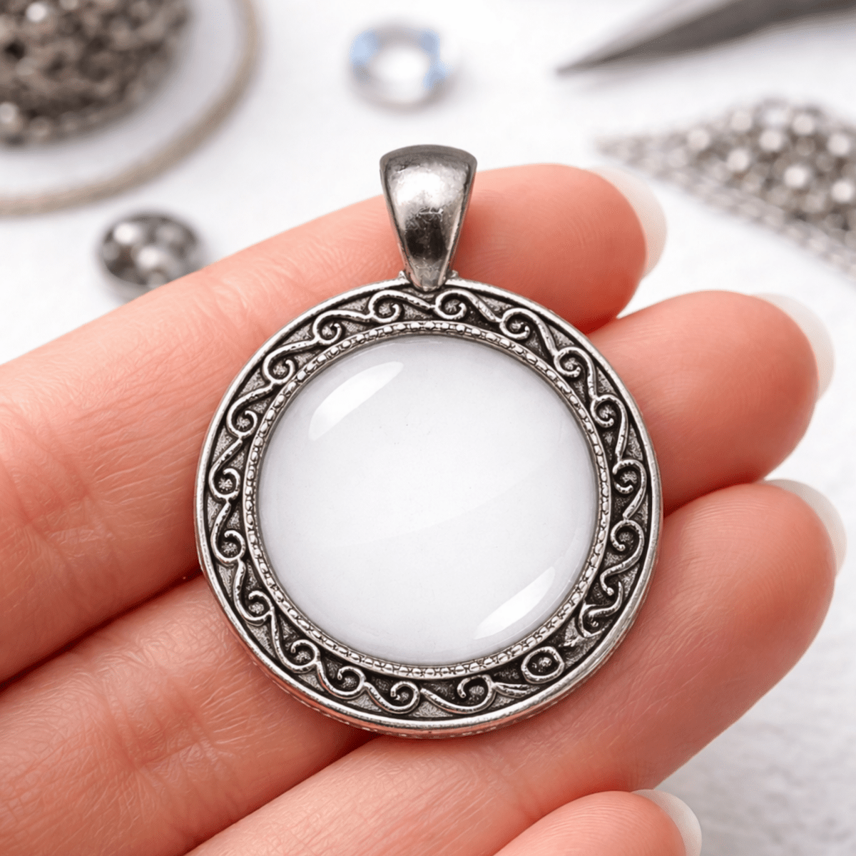 Silver pendant with white center held in hand against a blurred jewelry background