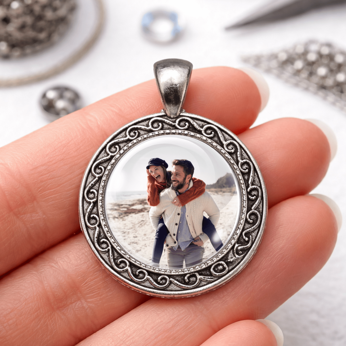 Silver pendant with a photo of a couple on a beach held in a hand.