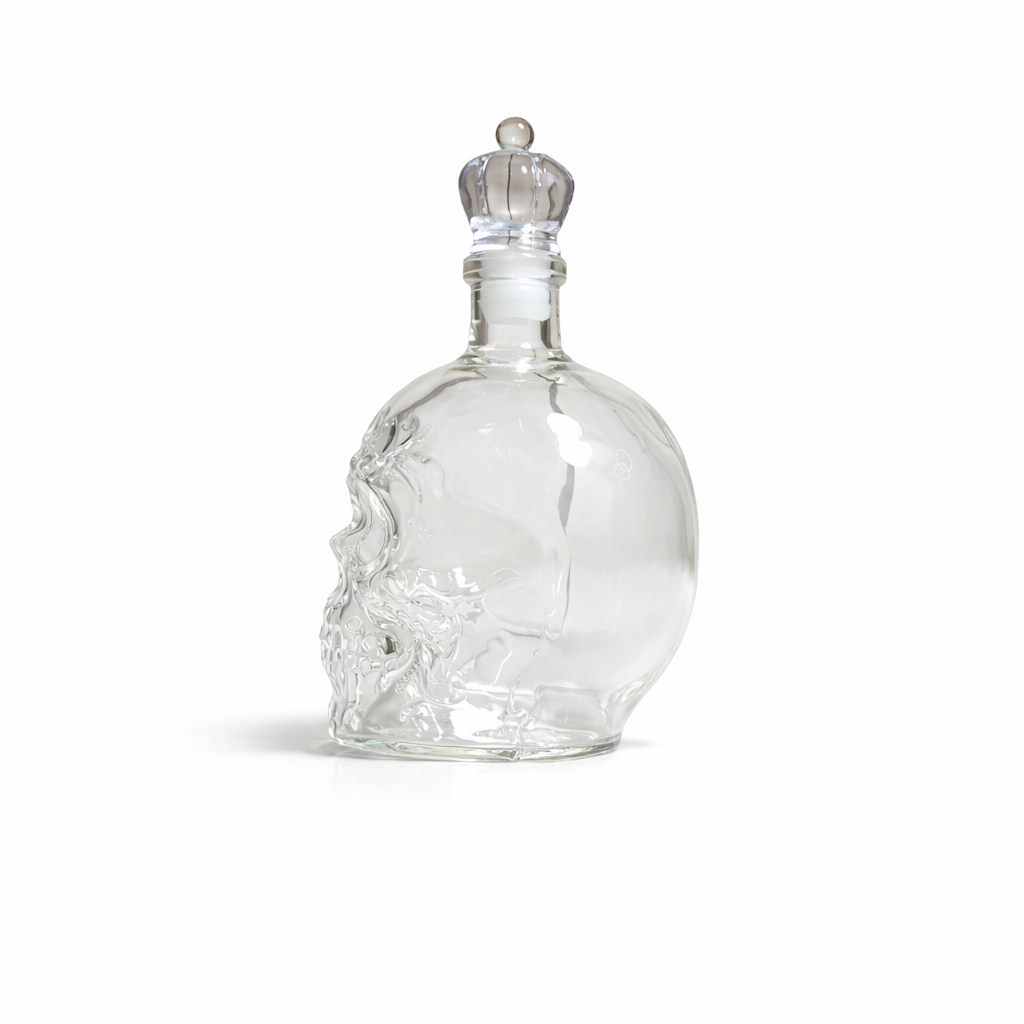 Clear glass skull-shaped bottle with a silver cap on a white background