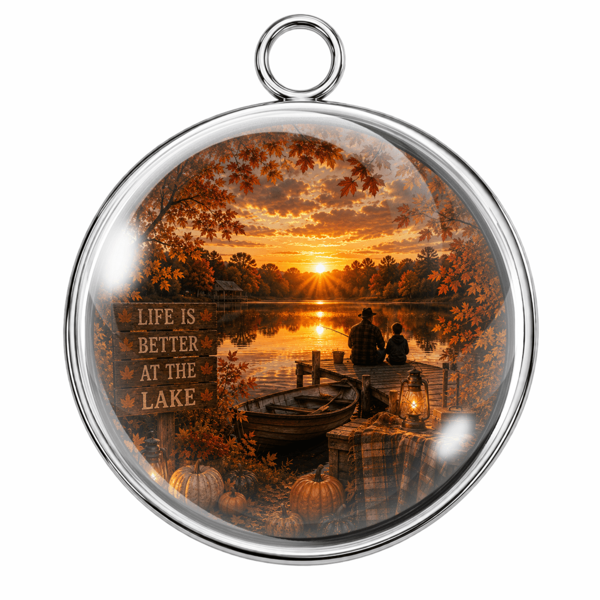 Round silver-toned pendant with a clear glass dome and a printed autumn lakeside sunset scene inside, featuring a dock, silhouetted figures, pumpkins, and a sign reading 'LIFE IS BETTER AT THE LAKE.'.