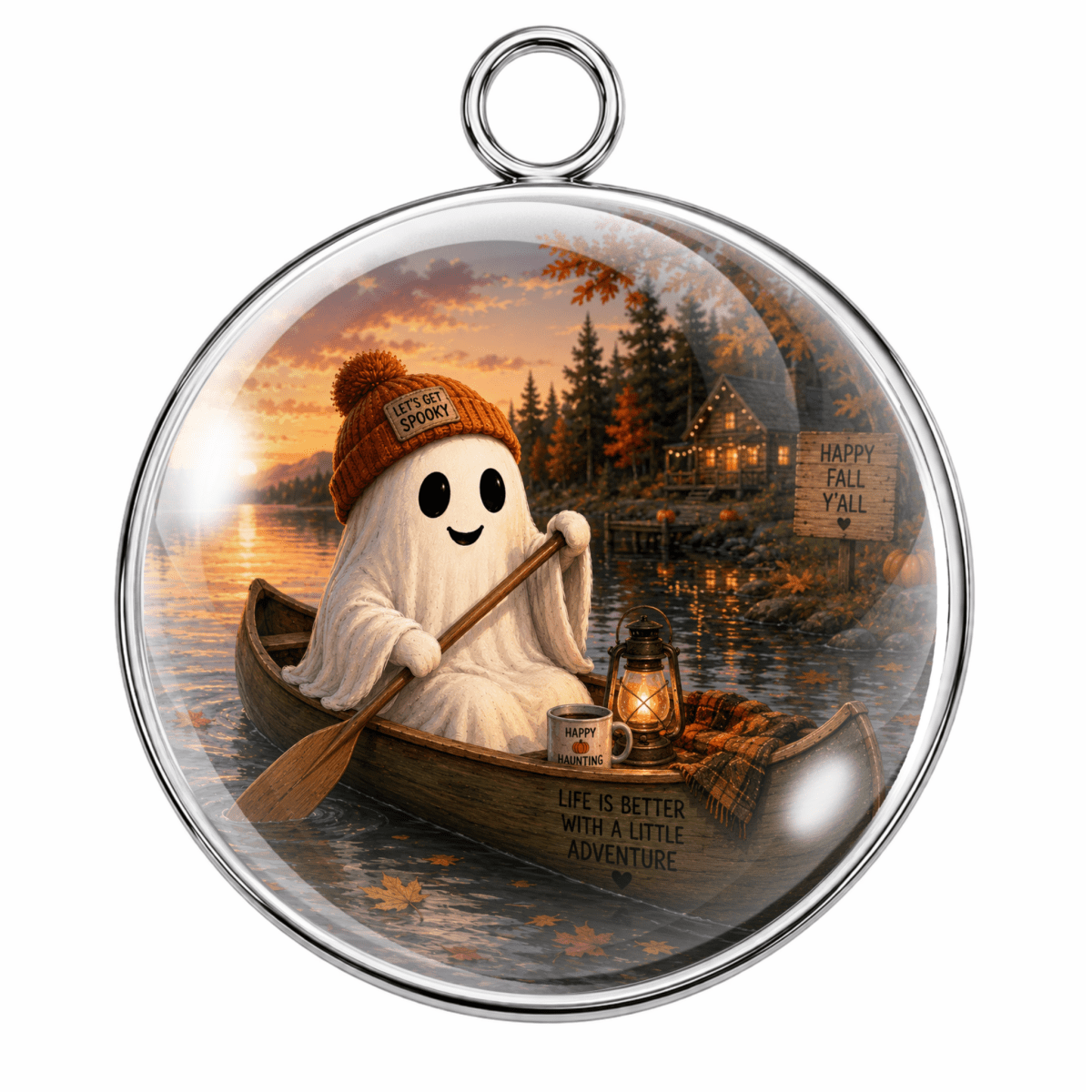 Round glass pendant ornament with a silver metal rim and hanging loop, featuring a whimsical illustration of a white ghost in an orange beanie rowing a canoe on a lake at sunset, with a lantern, mug, trees, and a house in the background.
