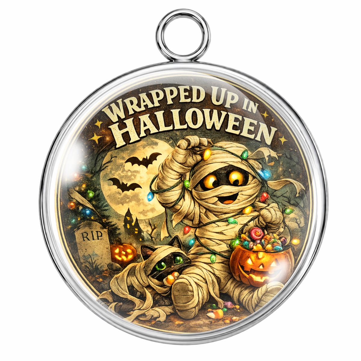 A round silver-toned pendant with a hanging loop at the top and a Halloween-themed illustrated design inside. The artwork shows a mummy wrapped in string lights, a small cat, pumpkins, bats, a full moon, and the text 'WRAPPED UP IN HALLOWEEN' across the top.