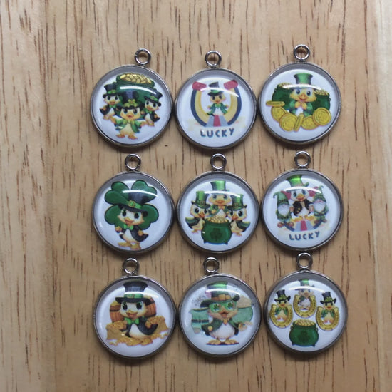 video of 9 glass cabochon charms with ducks in st Patricks clothing in front of gold