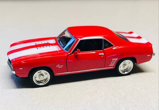 A red die-cast model car with white racing stripes, resembling a classic muscle car, displayed on a light gray surface with a wooden background.