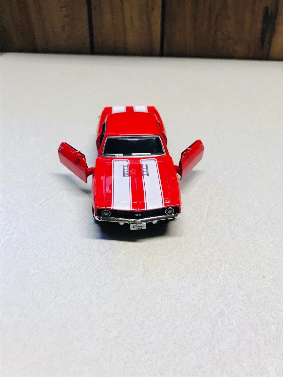 A red die-cast model car with white racing stripes and open doors, photographed on a light surface with a dark wood background.