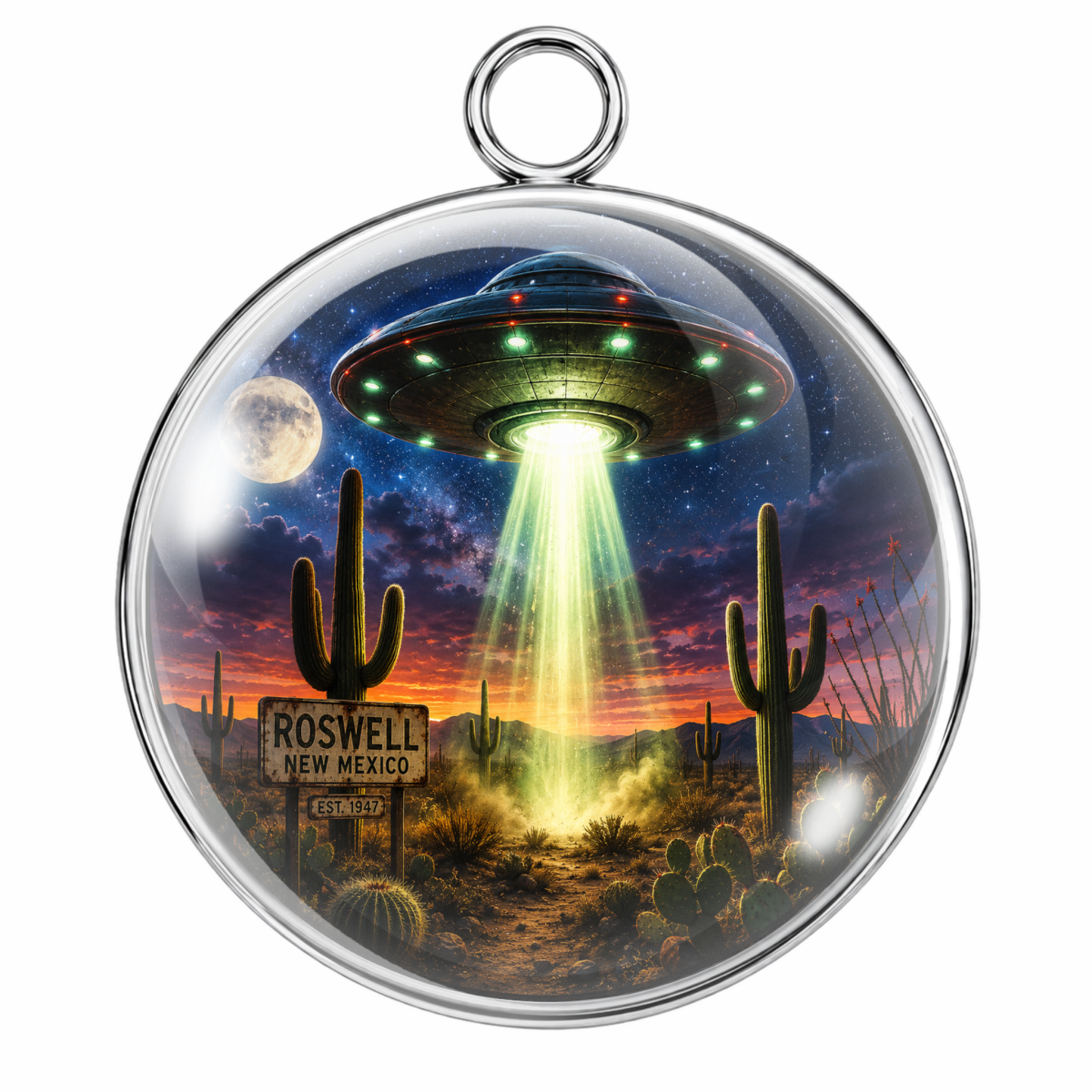 A round pendant with a silver-tone metal rim and hanging loop, featuring a printed desert night scene with a UFO, glowing beam, cacti, stars, and a moon. The sign in the scene reads Roswell New Mexico.