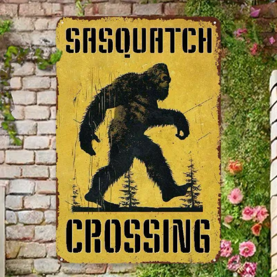 Vintage-style 'Sasquatch Crossing' sign with a yellow background and black text, featuring an illustration of a bigfoot.