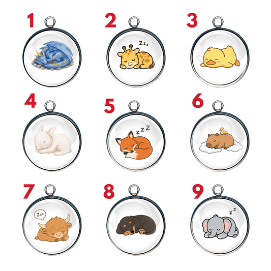 Nine cute sleepy animal glass cabochon charms featuring a blue dragon, giraffe, duckling, white rabbit, orange fox, capybara with a duckling, Highland cow, black-and-tan puppy, and gray elephant.