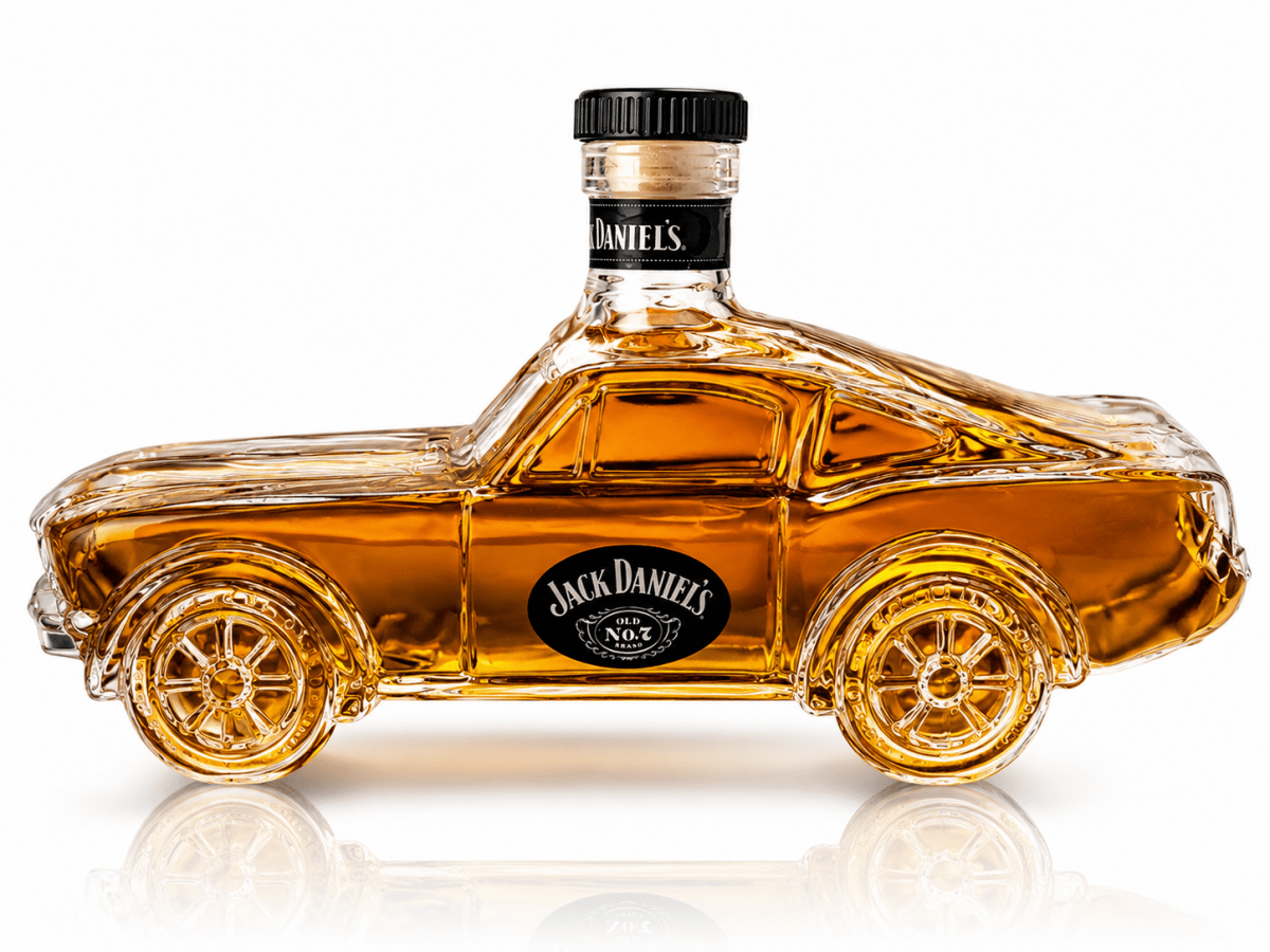 A Jack Daniel's branded clear glass bottle shaped like a classic car, filled with amber whiskey, shown on a white background with a reflection below.