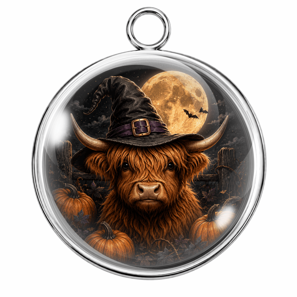 A round silver-toned pendant with a hanging loop, featuring a printed Halloween illustration of a shaggy Highland cow wearing a witch hat in front of a full moon and pumpkins.