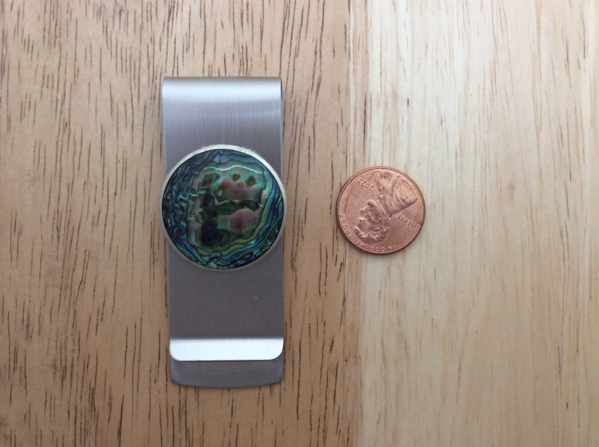 stainless steel money clip with a abalone setting next to a penny