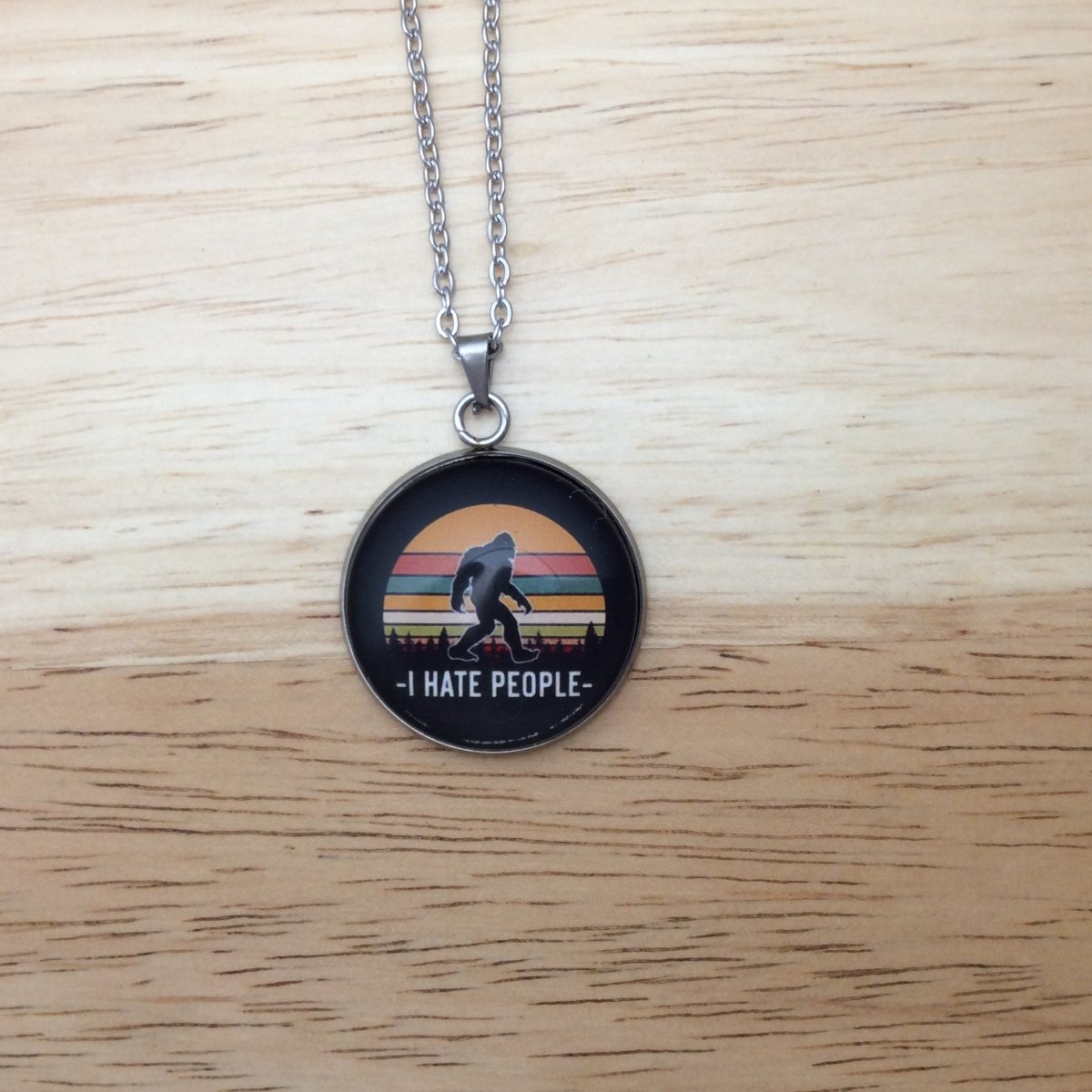 Stainless steel necklace with a glass cabochon pendant that Showa a Bigfoot walking in front of a colorful moon and it says "I Hate People"