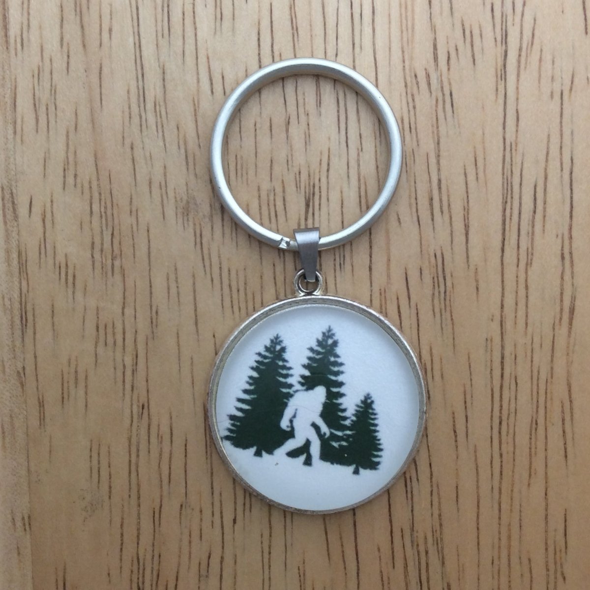 Tibetan silver glass cabochon keyring with a bigfoot walking in front of Green Pine Trees.