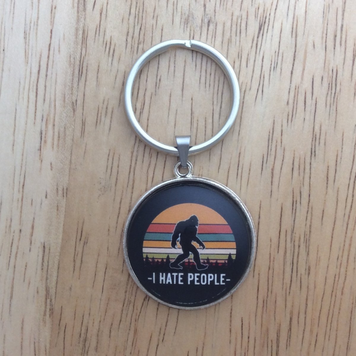 Tibetan silver glass cabochon keyring with a bigfoot walking in front of a multi colored moon and says "I Hate People"