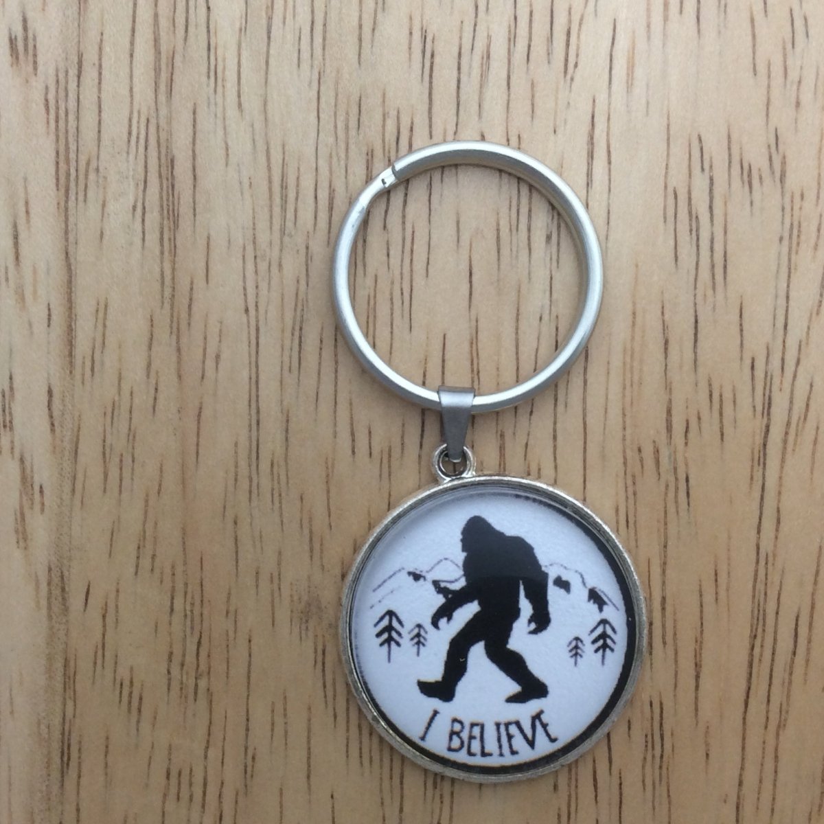 Tibetan silver glass cabochon keyring with a bigfoot walking in front of mountains and says "I Believe"