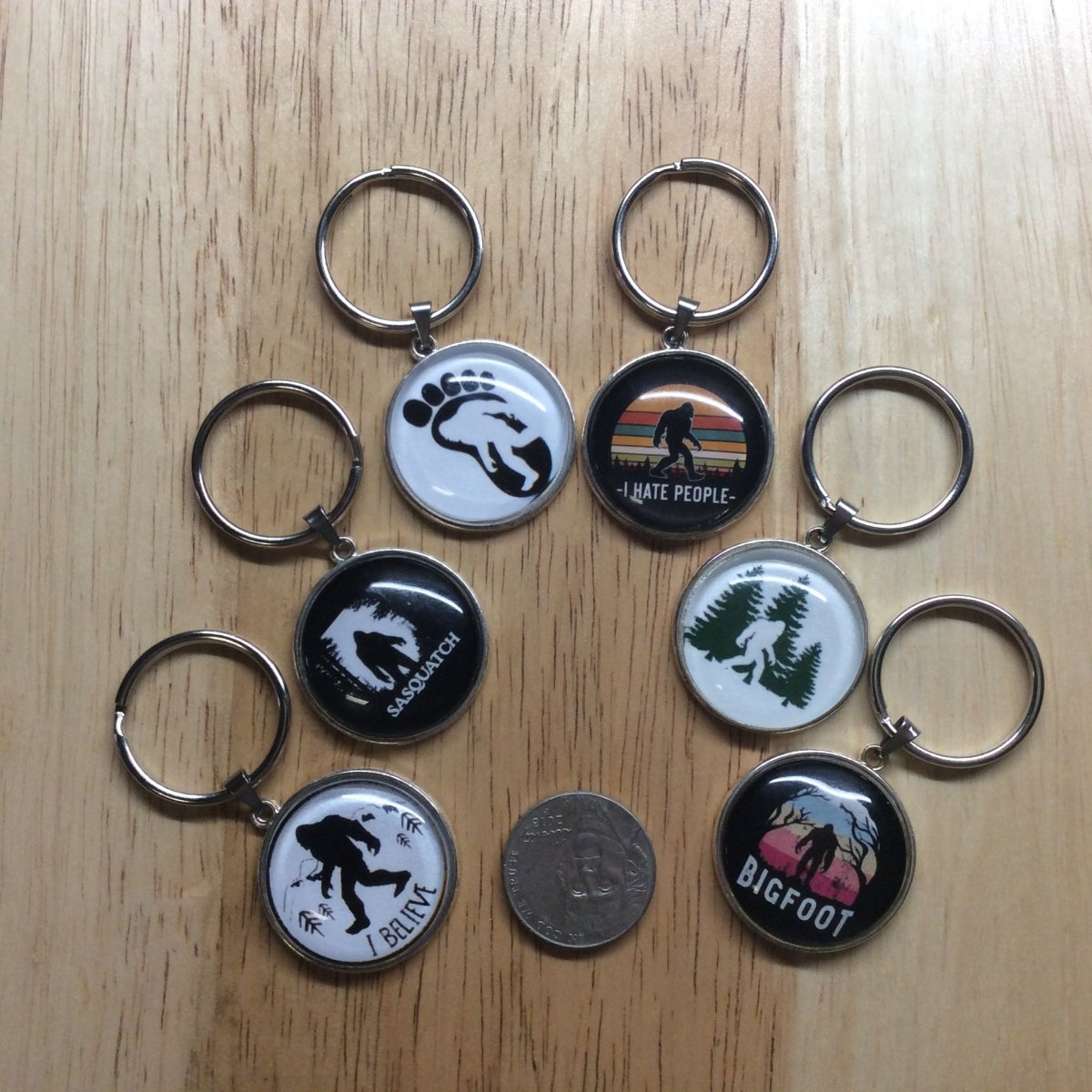 9 tibetan silver glass cabochon keyring with various bigfoot scenes and a nickel as reference to show the size.