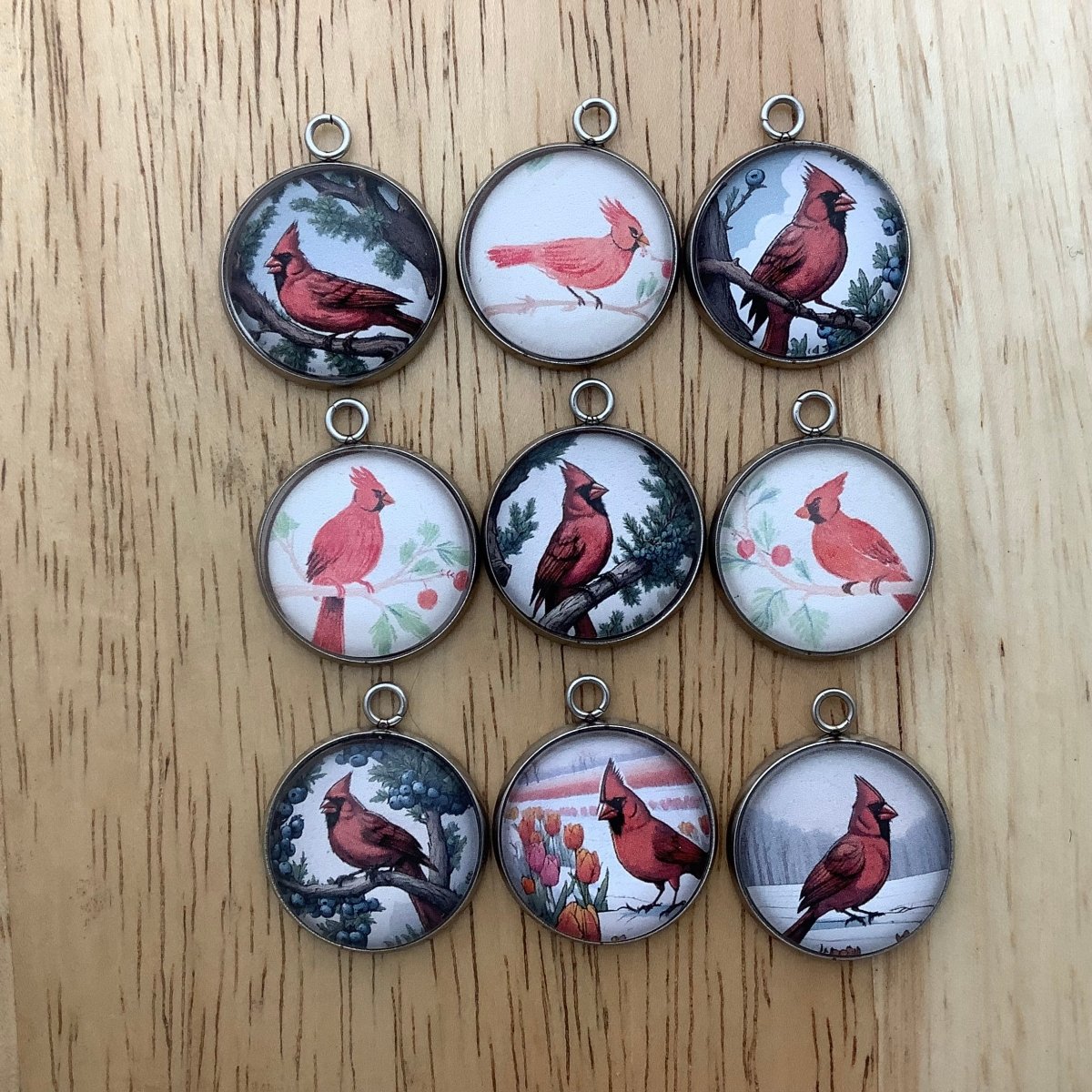 Group of 9 charms depicting cardinals on a branch or on the ground