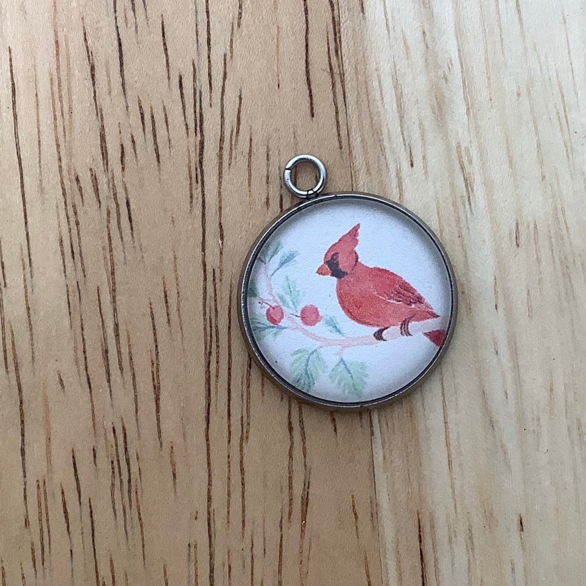 a charm of a color pencil drawn cardinal on a branch with red berries