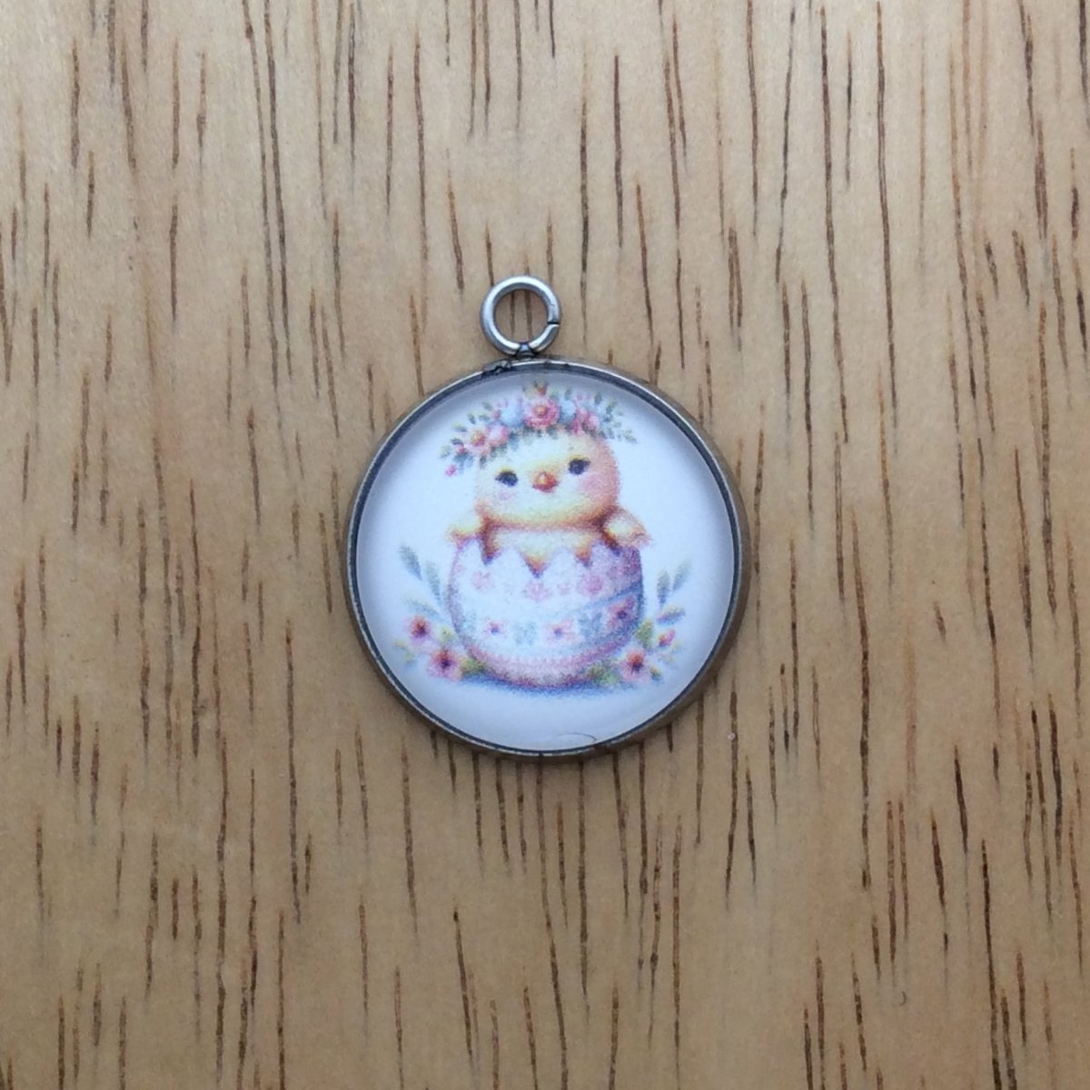 A glass cabochon charm with a baby chick inside