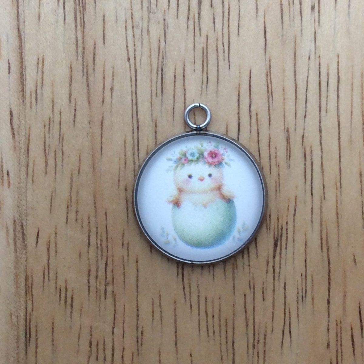 A glass cabochon charm with a baby chick inside