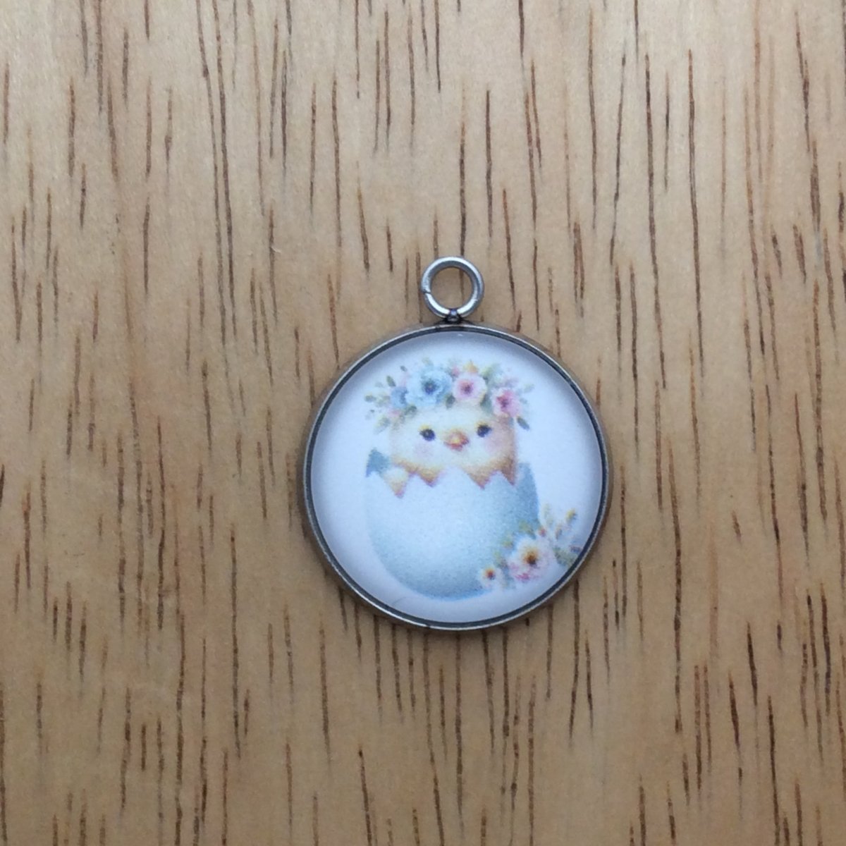 A glass cabochon charm with a baby chick inside