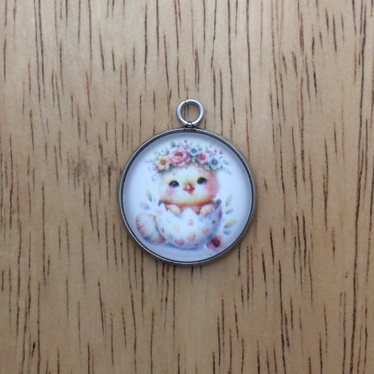 A glass cabochon charm with a baby chick inside