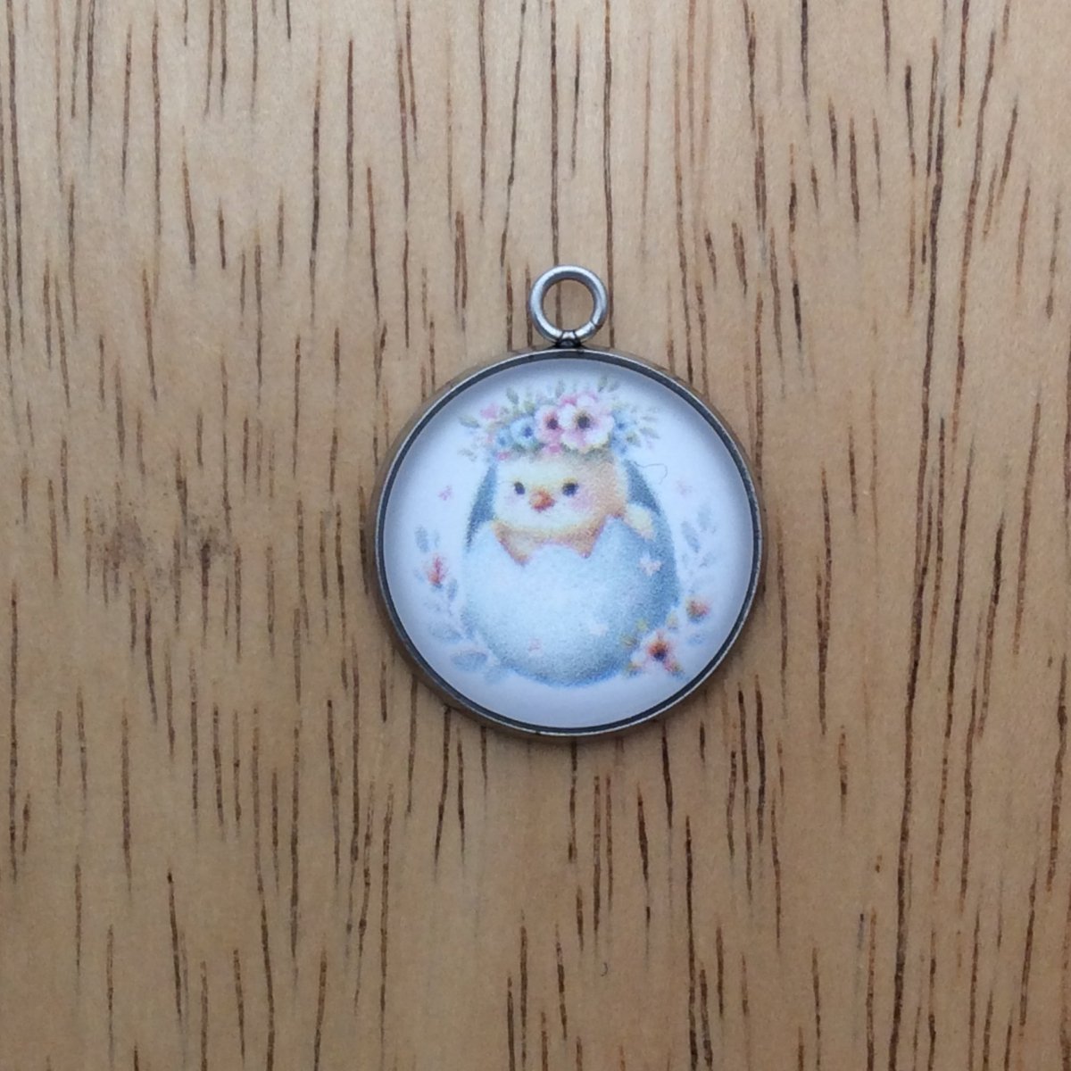 A glass cabochon charm with a baby chick inside