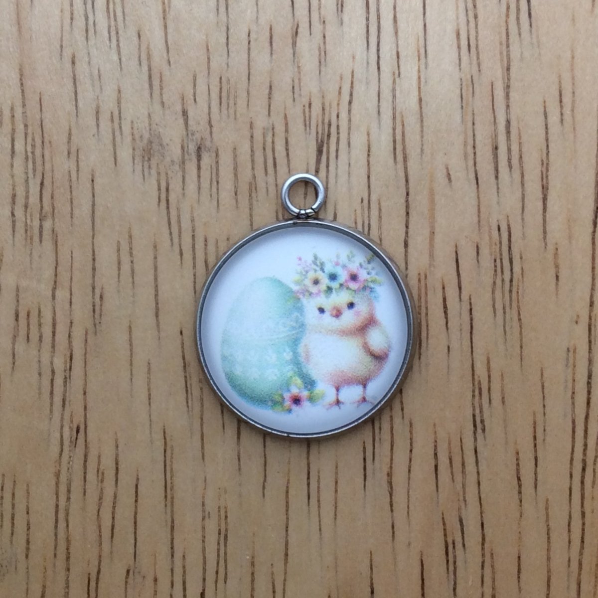 A glass cabochon charm with a baby chick inside