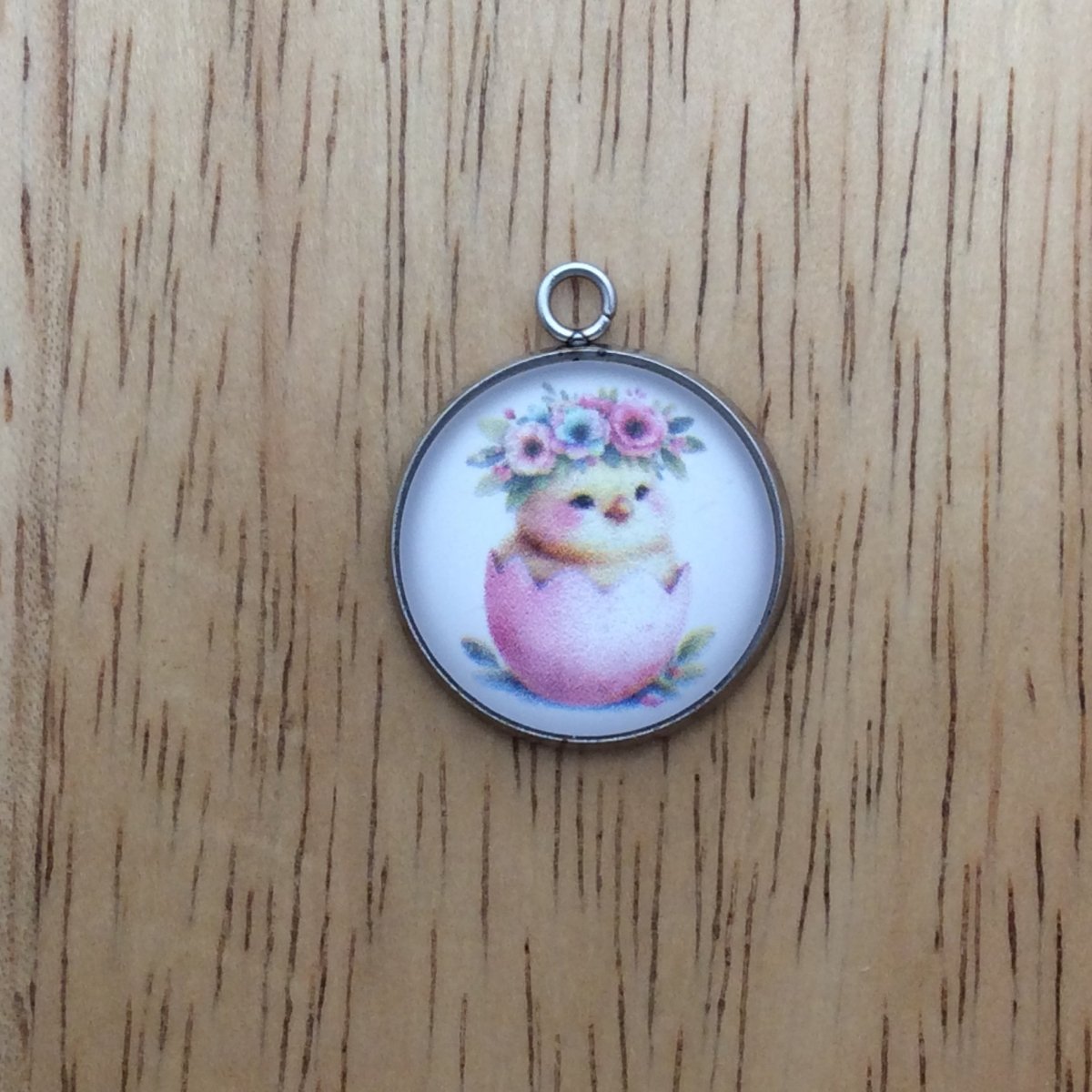 A glass cabochon charm with a baby chick inside