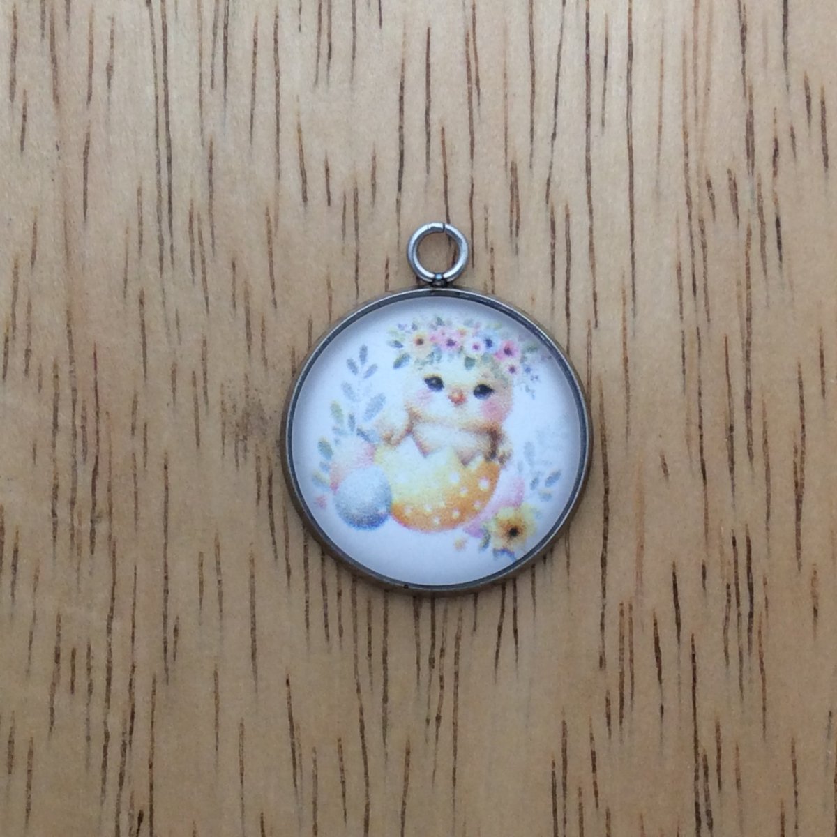 A glass cabochon charm with a baby chick inside