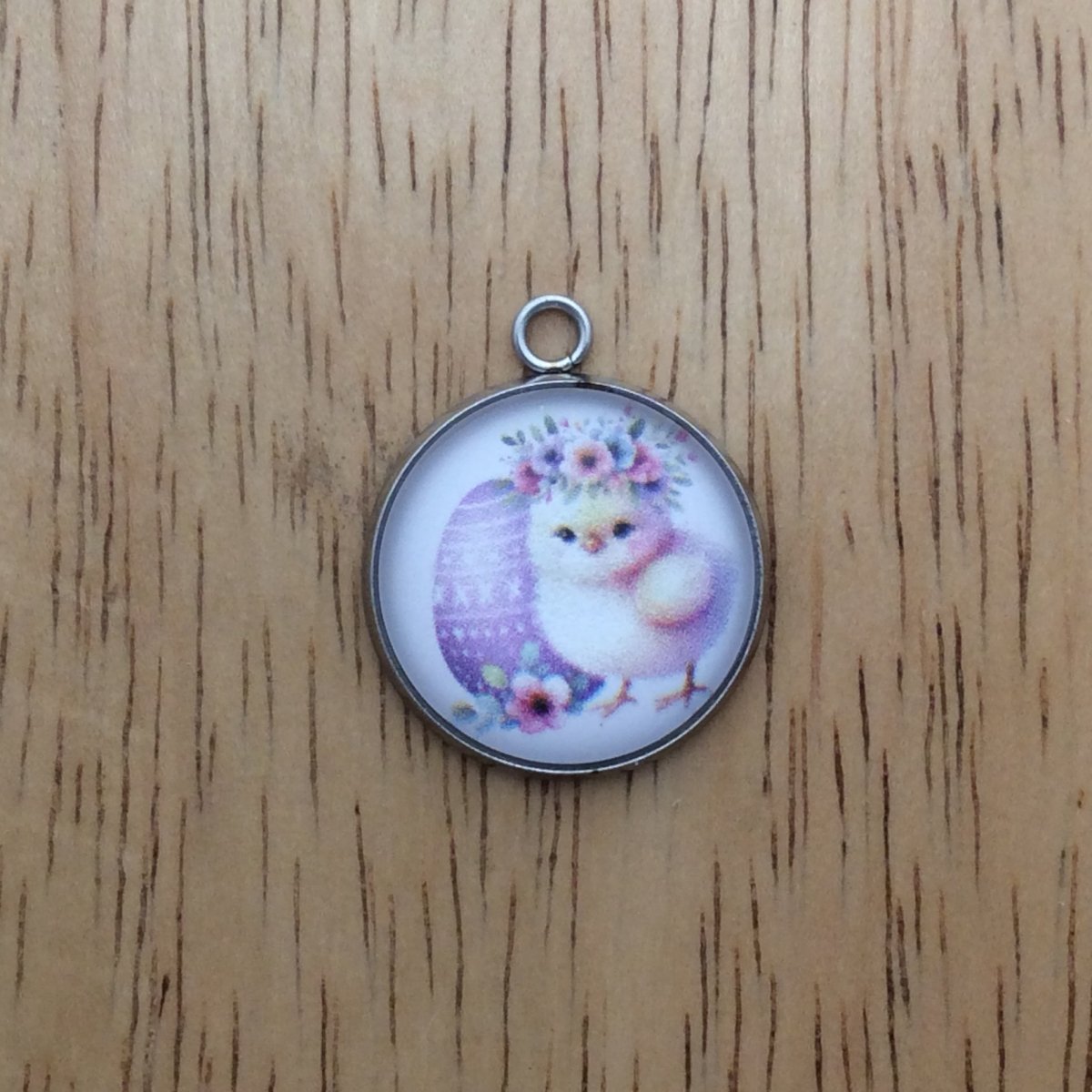 A glass cabochon charm with a baby chick inside