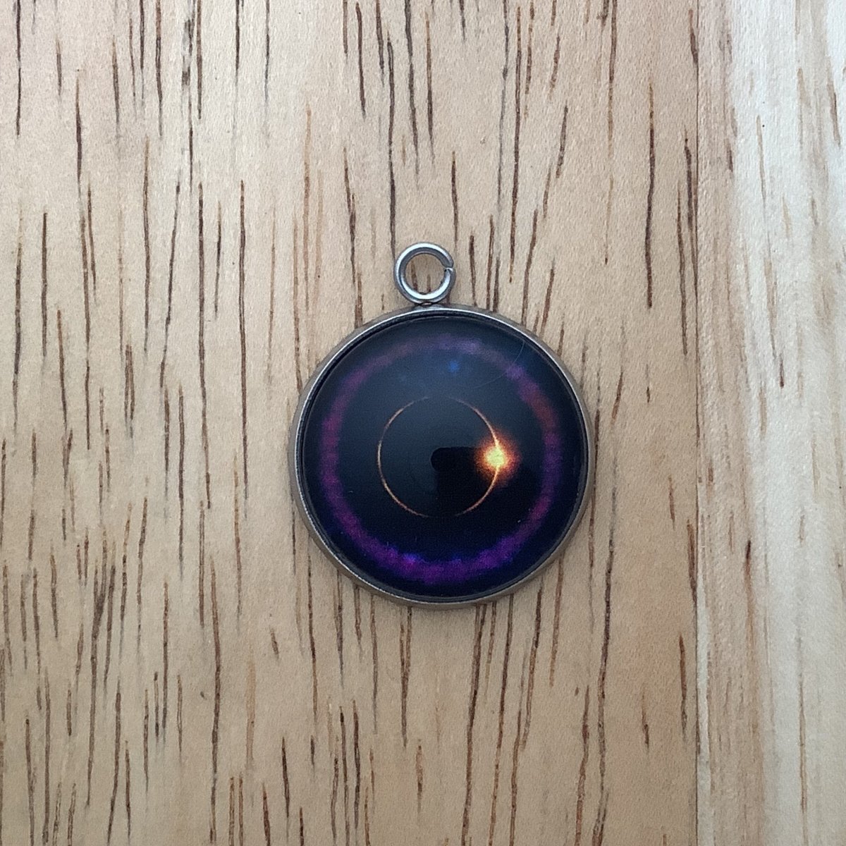 a charm depicting an eclipse witha purple ring