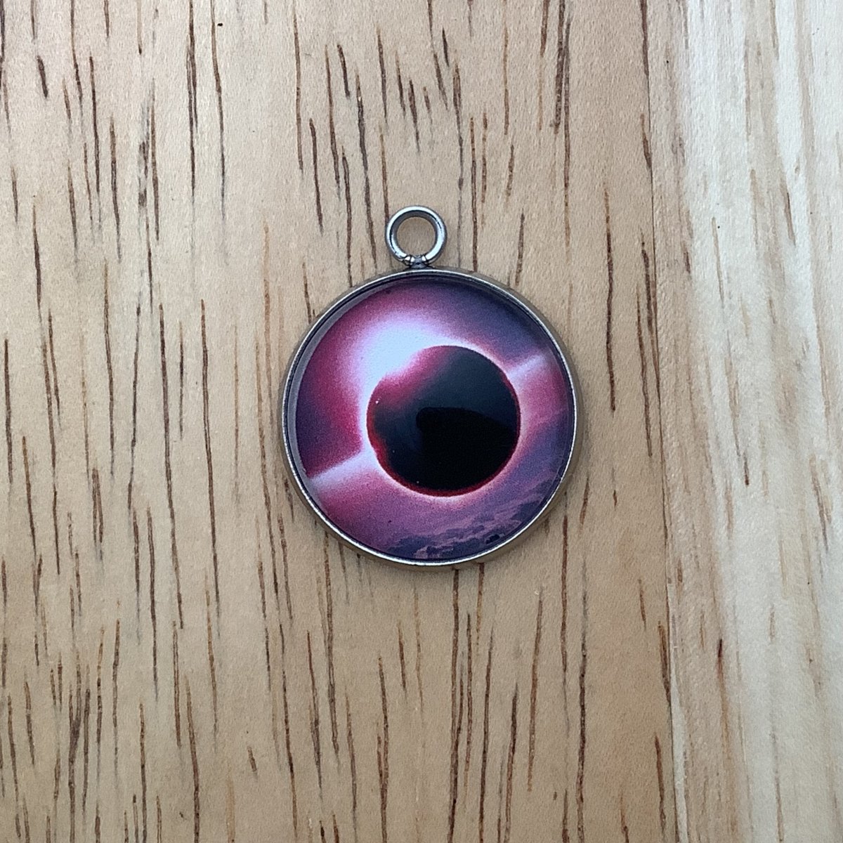 a charm depicting an eclipse with a pink skyline background