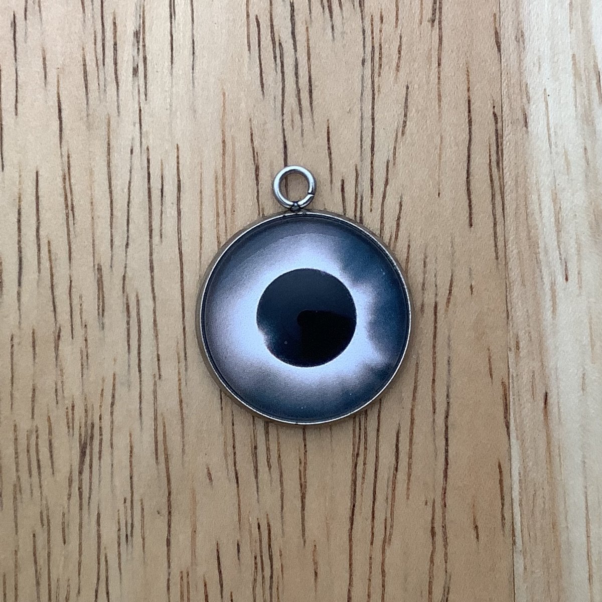 a charm depicting an eclipse with a bright lights in the background